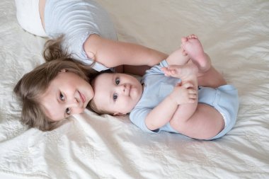 girl older sister hugging her little baby boy brother on bed at home.
