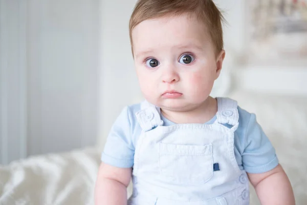 close up portrait baby boy 6 months old in blu clothes smiling and sitting on white bed at home