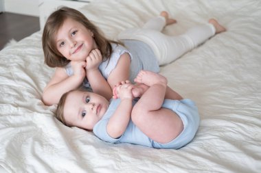 girl older sister lying on bed with her little baby boy brother at home.