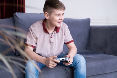 Heyecanlı genç oyuncu çocuk oyun oynuyor, joystick ile oyun oynuyor, evdeki kanepede oturuyor..