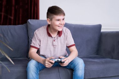 Heyecanlı genç oyuncu çocuk oyun oynuyor, joystick ile oyun oynuyor, evdeki kanepede oturuyor.