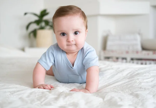 Funny baby boy 6 months old in blu bodysuit smiling and lying on bed at home. — Stock Photo, Image