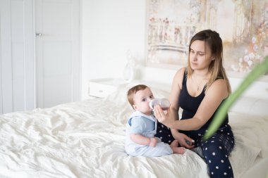 Genç anne bebeğini şişeden besliyor. Anne bebeğine içki veriyor.