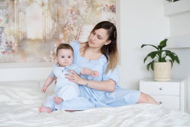 Güzel bir kadın anne oğlunu kucağında tutuyor. Evde yatakta oturuyor.