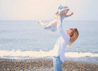 Anne küçük oğlunu havaya fırlattı, aile güneşli bir günde deniz kıyısında eğleniyor..