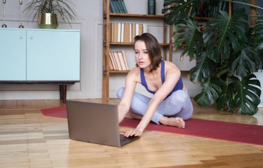Spor kıyafetli genç bir kadın evdeki bilgisayarında yoga egzersizleri izliyor..