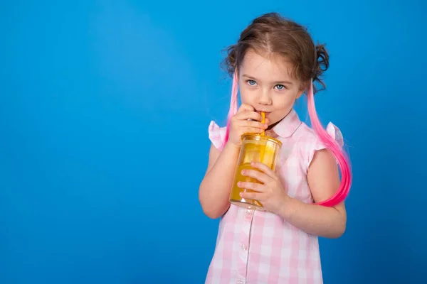 面白いです子供の女の子でピンクの服笑顔ホールディングガラスのオレンジジュースオン青の背景 — ストック写真