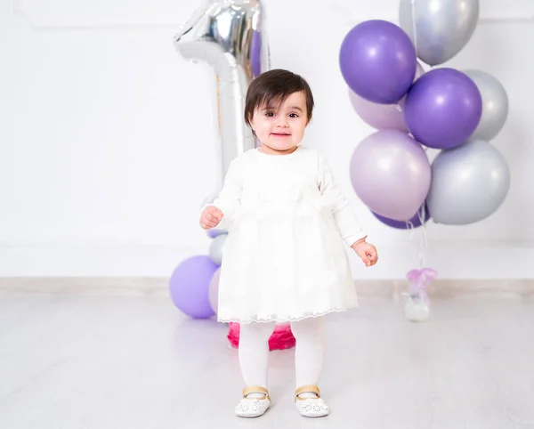 Beyaz elbiseli bebek ilk doğum gününü pasta ve balonlarla kutluyor..