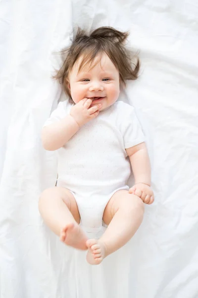 funny baby boy in white bodysuit smiling and lying on a white bedding at home. top view