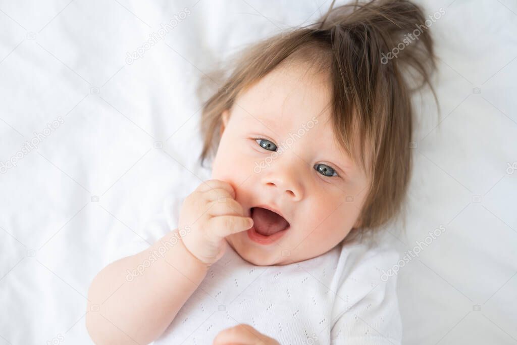 portrait of funny baby boy with finger in a mouth smiling and lying on a white bedding at home