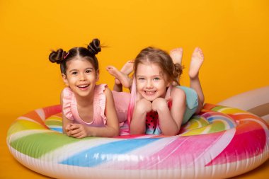 Renkli şişme yatakta uzanan mayolu iki mutlu kız sarı arka planda lolipop.