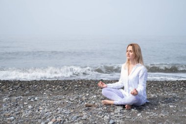 Genç kadınlar, plajda meditasyon pozisyonunda yoga yapıyorlar..