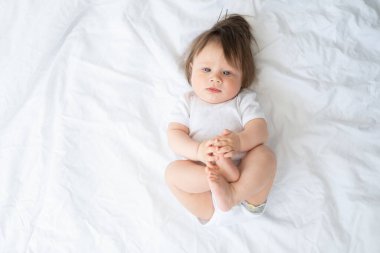 Beyaz elbiseli komik erkek bebek evde beyaz bir yatakta gülümsüyor ve yatıyor. en üstteki görünüm