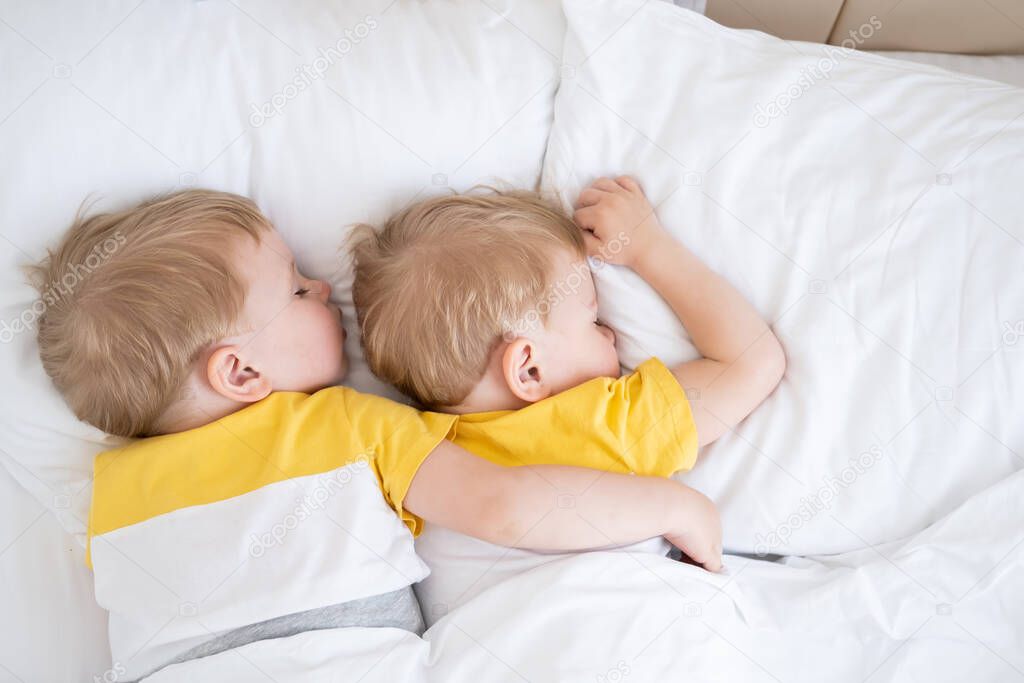 two blonde boys twins sleeping hugging on white bedding .