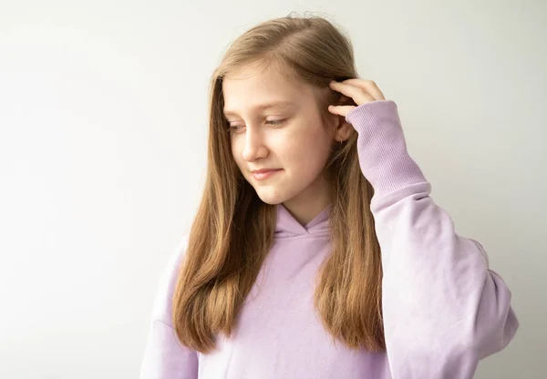 Krásná dospívající dívka s dlouhými vlasy ve fialové huddyhoodie dotýká její vlasy stojící proti bílé zdi — Stock fotografie