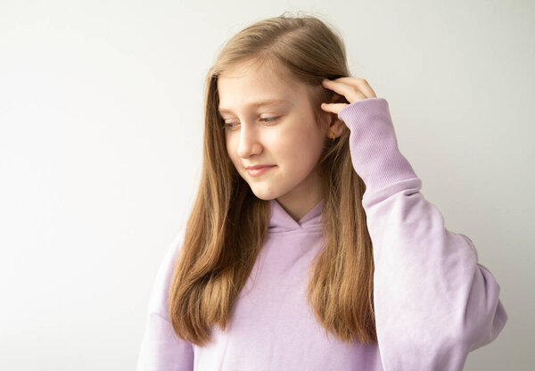 beautiful teenage girl with long hair in purple huddyhoodie touching her hair standing against white wall