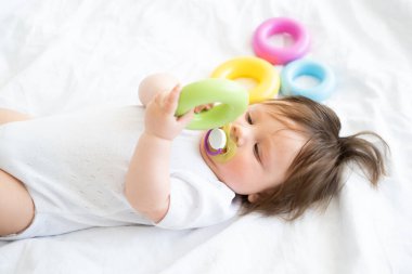 sağlıklı erkek bebek yatakta uzanıyor ve renkli plastik daire oyuncağıyla oynuyor