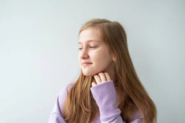Портрет красивой девушки-подростка с длинными волосами в фиолетовой толстовке, стоящей напротив белой стены — стоковое фото
