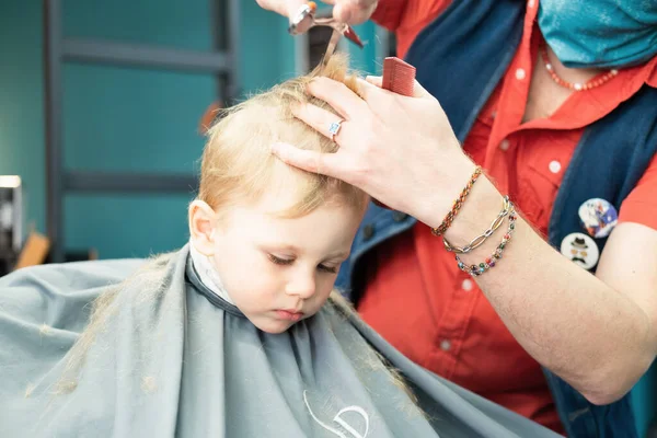 Cute little boy getting the first haircut in barbershop — Stock Photo, Image