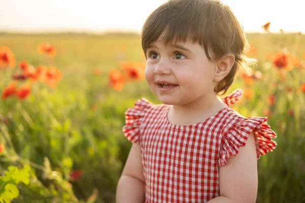 Крупным планом красивая счастливая девочка в красном платье, улыбающаяся на маковом поле на летнем закате — стоковое фото