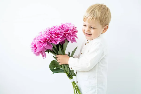 Enfant blond garçon avec grand bouquet de pivoines roses sur fond blanc. Amour et concept romantique — Photo