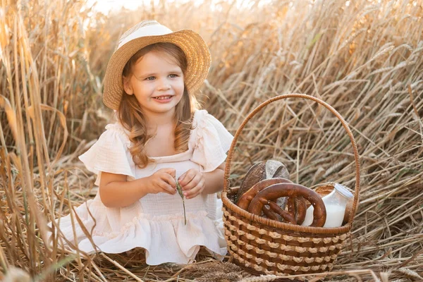 stock image little blonde girl in straw hat with basket of bread in wheat field. eco friendly farm products.