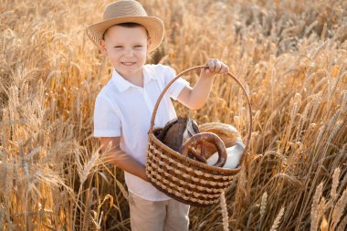 Hasır şapkalı çocuk buğday tarlasında bir sepet ekmek tutuyor. Çevre dostu tarım ürünleri.