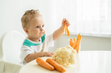 Bebek çocuk Childs sandalyesinde oturup beyaz arka planda havuç dilimleri yiyor..
