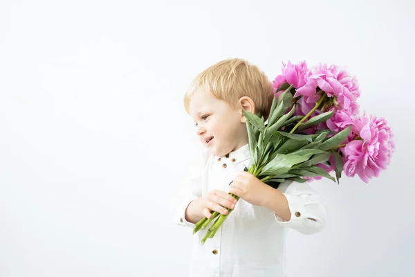 Мальчик блондин с большим букетом розовых пионов на белом фоне. Любовь и романтика — стоковое фото