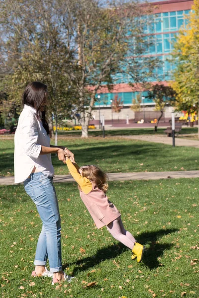 Szczęśliwa matka trzyma córkę za ręce i wiruje ją, dziecko lata i śmieje się — Zdjęcie stockowe