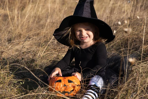 Vicces kisbaba lány fekete boszorkány kalap narancs cukorka vödör a természetben. — Stock Fotó