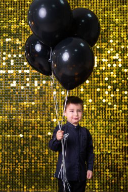 Arkaplanda altın rengi pullar ve kovalarla siyah balonlar tutan çocuk.