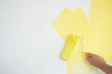 Duvarı sarı renkli silindirle boyayan adam. Yenileme, onarım ve yeniden dekorasyon konsepti.
