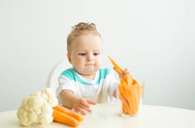 Bebek çocuk Childs sandalyesinde oturup beyaz arka planda havuç dilimleri yiyor.