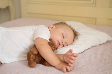 Evdeki yatakta uyuyan komik çocuk. Çocuk kucaklayan oyuncak ayı.