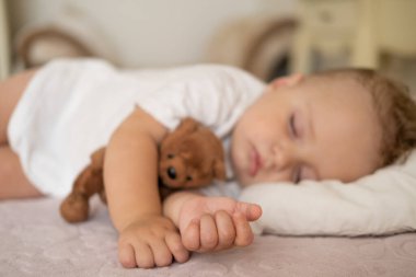 Evdeki yatakta uyuyan komik çocuk. Çocuk kucaklayan oyuncak ayı. ellere odaklan