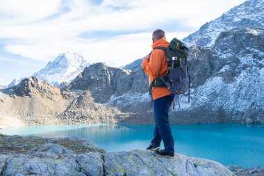 Gölün yukarısındaki kayalıklarda ağır sırt çantalı bir gezgin. Seyahat yaşam tarzı, macera