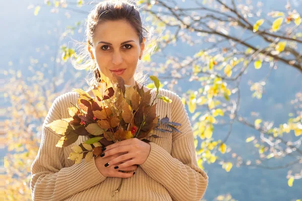 Ελκυστική ευτυχισμένη μεσήλικη γυναίκα σε πουλόβερ κρατά μπουκέτο από πολύχρωμα φύλλα. Φθινοπωρινή περίοδος. — Φωτογραφία Αρχείου