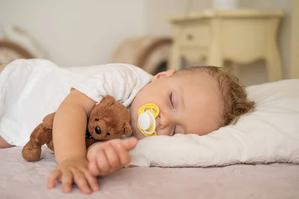 Lindo bebé con pezón durmiendo en la cama en casa. niño abrazando osito de peluche. Imagen De Stock