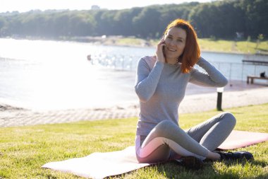 Parkta cep telefonu kullanan, spor elbiseli, zayıf kızıl bir kadın. Sağlık, sağlık, sağlık yaşam tarzı.