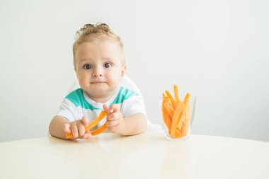 Bebek çocuk Childs sandalyesinde oturup beyaz arka planda havuç dilimleri yiyor.
