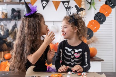 Cadı kostümü giymiş iki farklı çocuk mutfakta eğleniyor ve Cadılar Bayramı 'nı kutluyor..