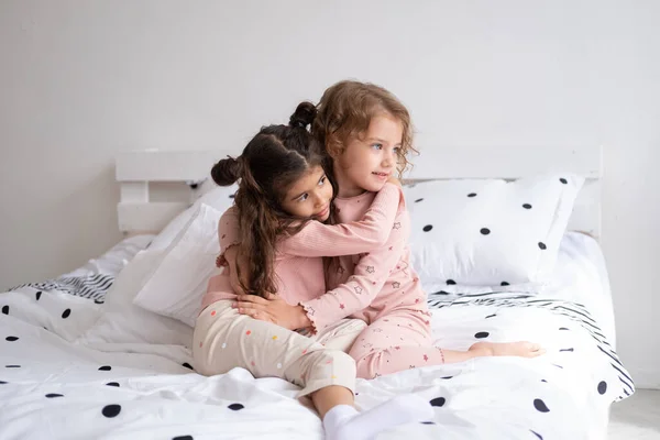 Duas Belas Crianças Diversas Meninas Pijama Abraçando Cama Moderno Apartamento — Fotografia de Stock