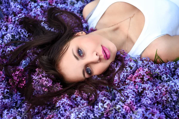 Jovem menina bonita encontra-se nas flores lilás . — Fotografia de Stock