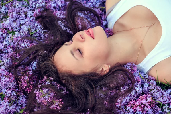 Молода красива дівчина лежить на бузкових квітах . — стокове фото