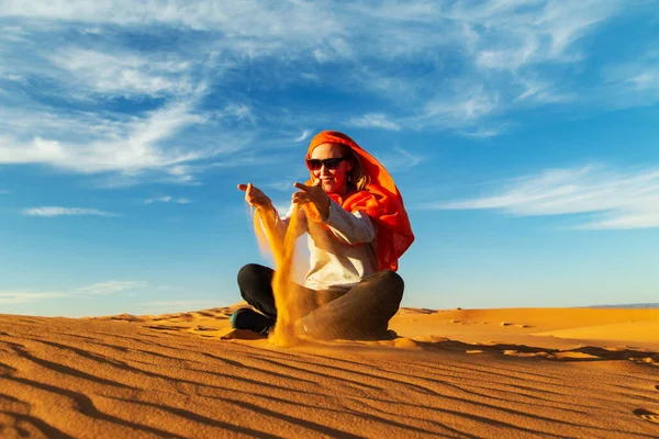 Girl plays with sand in the Sahara desert. Erg Chebbi, Merzouga,  Morocco.