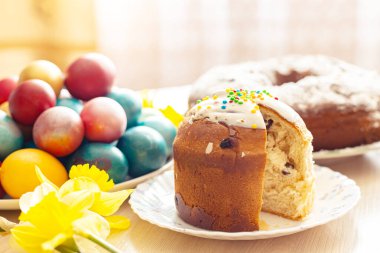 Dilimlenmiş Paskalya ortodoks tatlı ekmeği, kulich, renkli yumurta ve bir buket nergis. Parlak güneş ışığı. Geleneksel Paskalya kahvaltısı. Seçici odak.