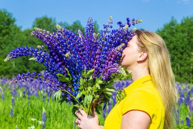 Lupin tarlasında sarı elbiseli sarışın bir kadın. Yaz güneşli bir gün. Rahatlama, tatil, özgürlük kavramı. 