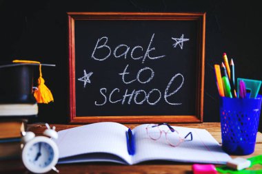 Masaüstünde kitaplar, yazma malzemeleri, gözlükler, not defteri ve çalar saat. Tebeşir harfleri 