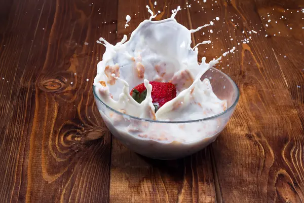 Fresa cayendo en un bol con leche y cereales . —  Fotos de Stock